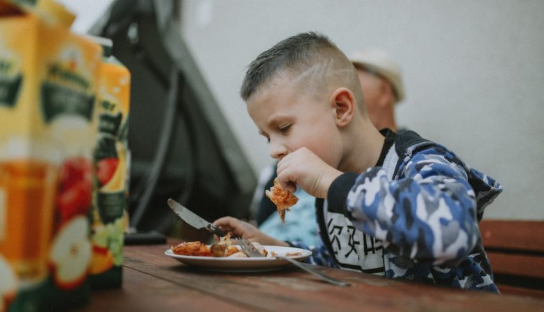 Young boy savoring a grilled chicken meal during an outdoor barbecue.